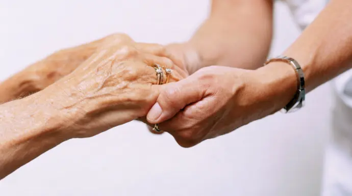 Una cuidadora sostiene las manos de una persona mayor