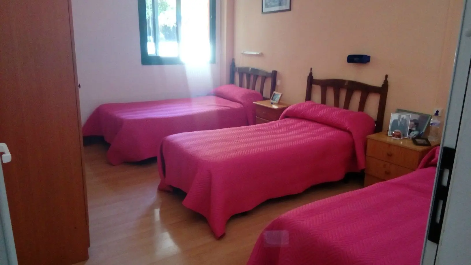 Habitación triple con tres camas, mesillas y ventana exterior con luz natural
