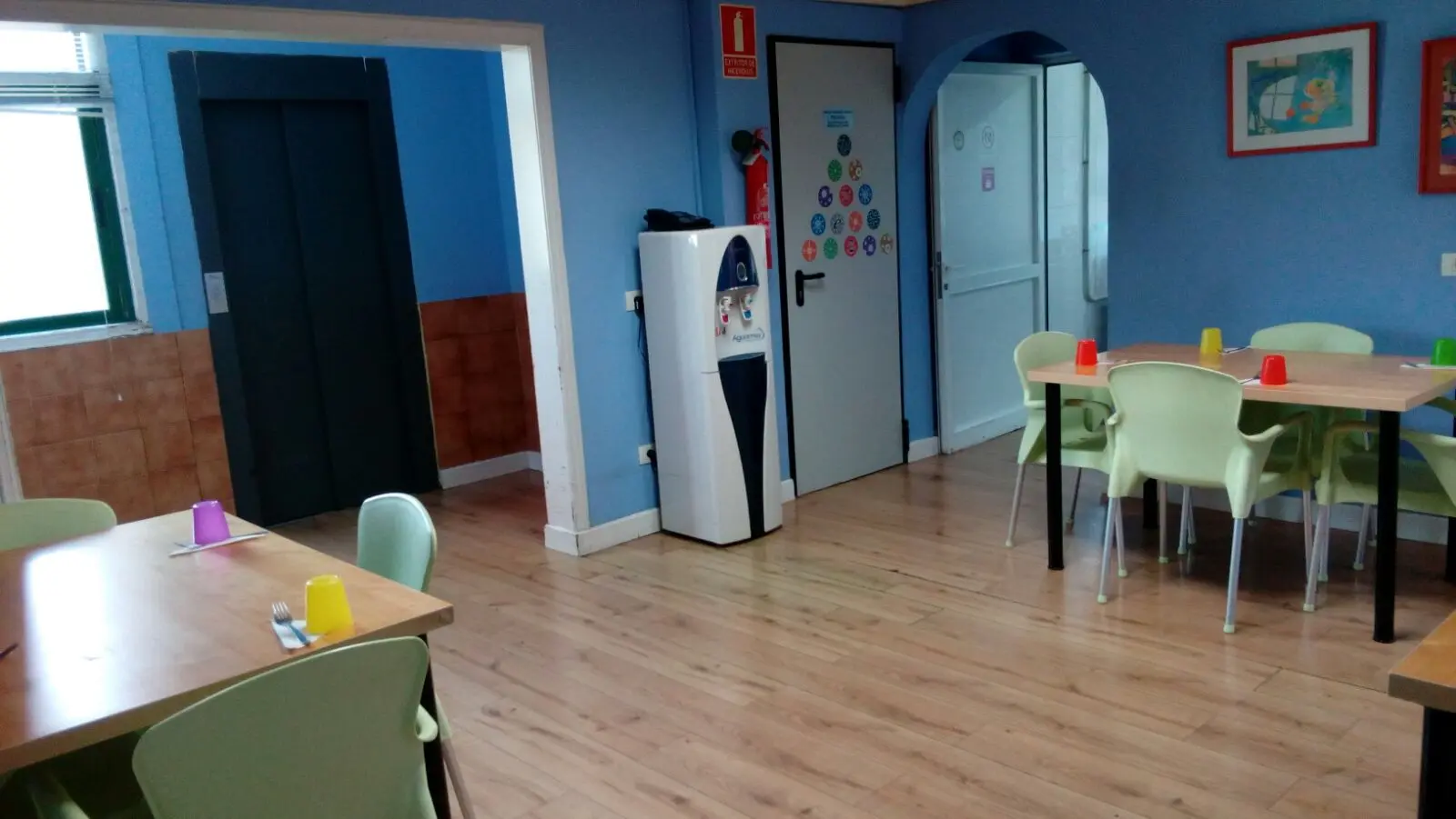 Comedor con mesas y sillas junto al ascensor y dispensador de agua