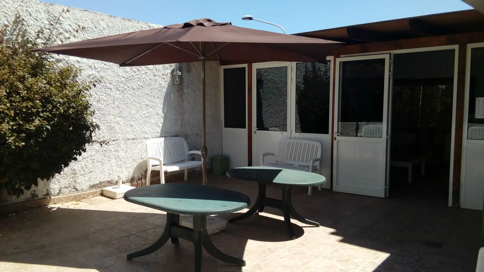 Terraza soleada con sombrilla, mesas y bancos blancos a la sombra