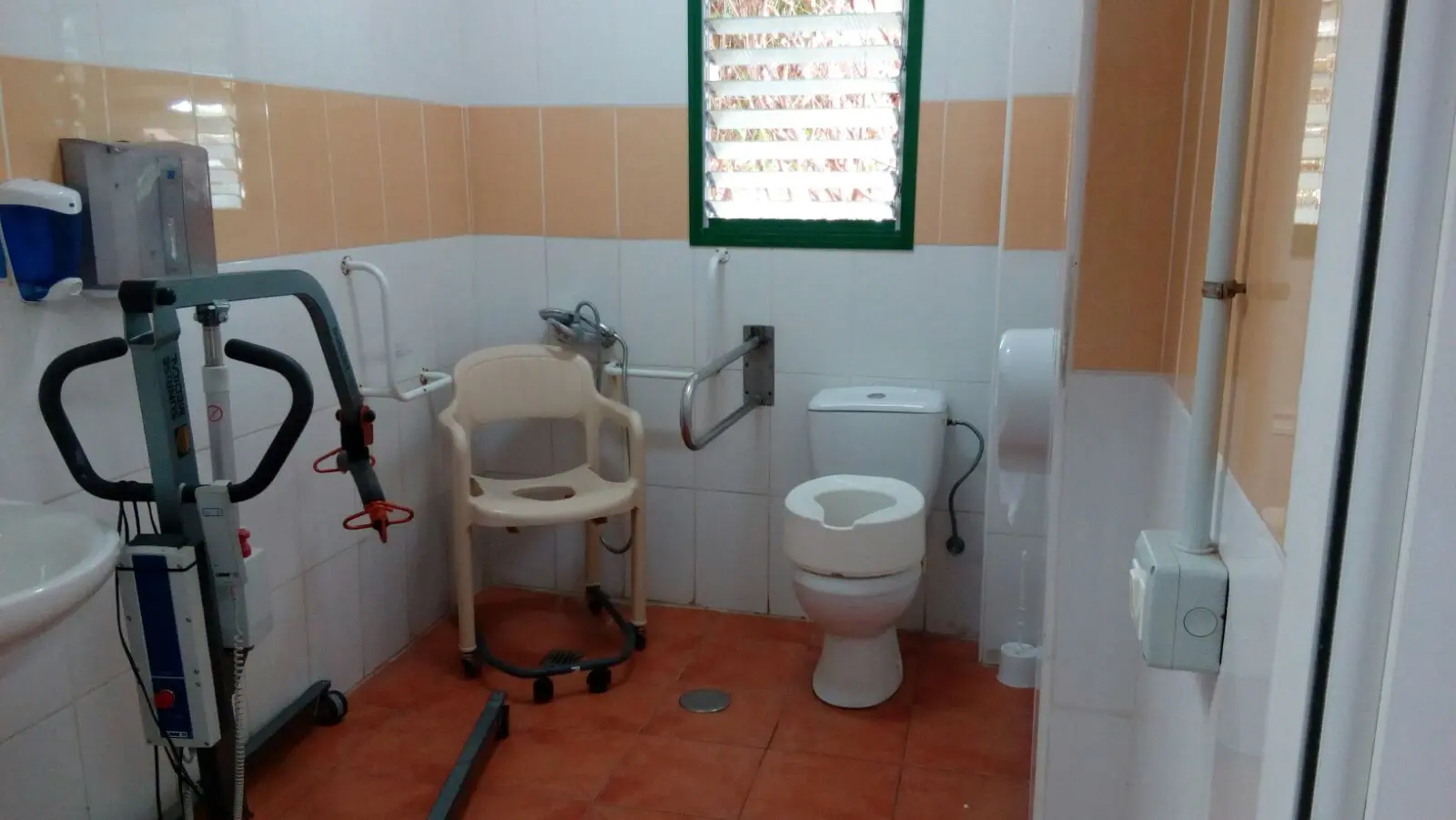 Baño adaptado con grúa de traslado, silla de ducha, asideros y inodoro elevado