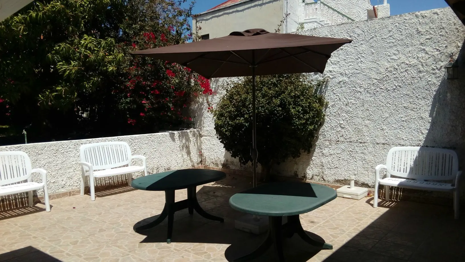 Terraza con sombrilla y bancos rodeada de buganvillas en flor